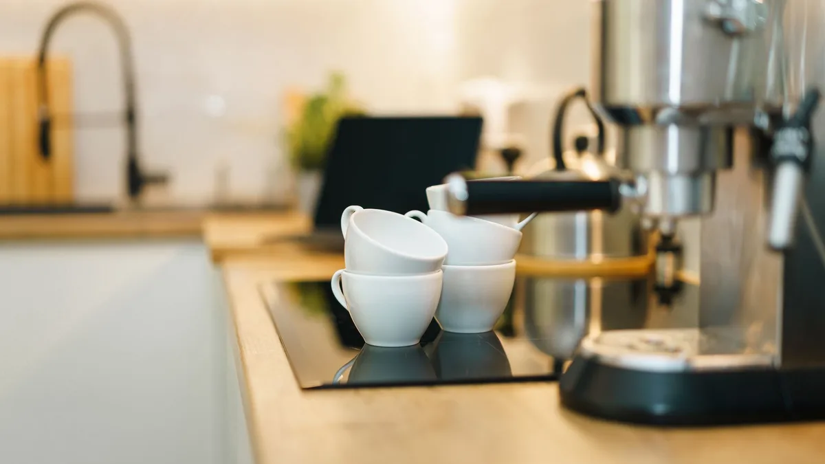 Cafetera espresso de acero sobre una encimera de madera junto a un grupo de tazas blancas