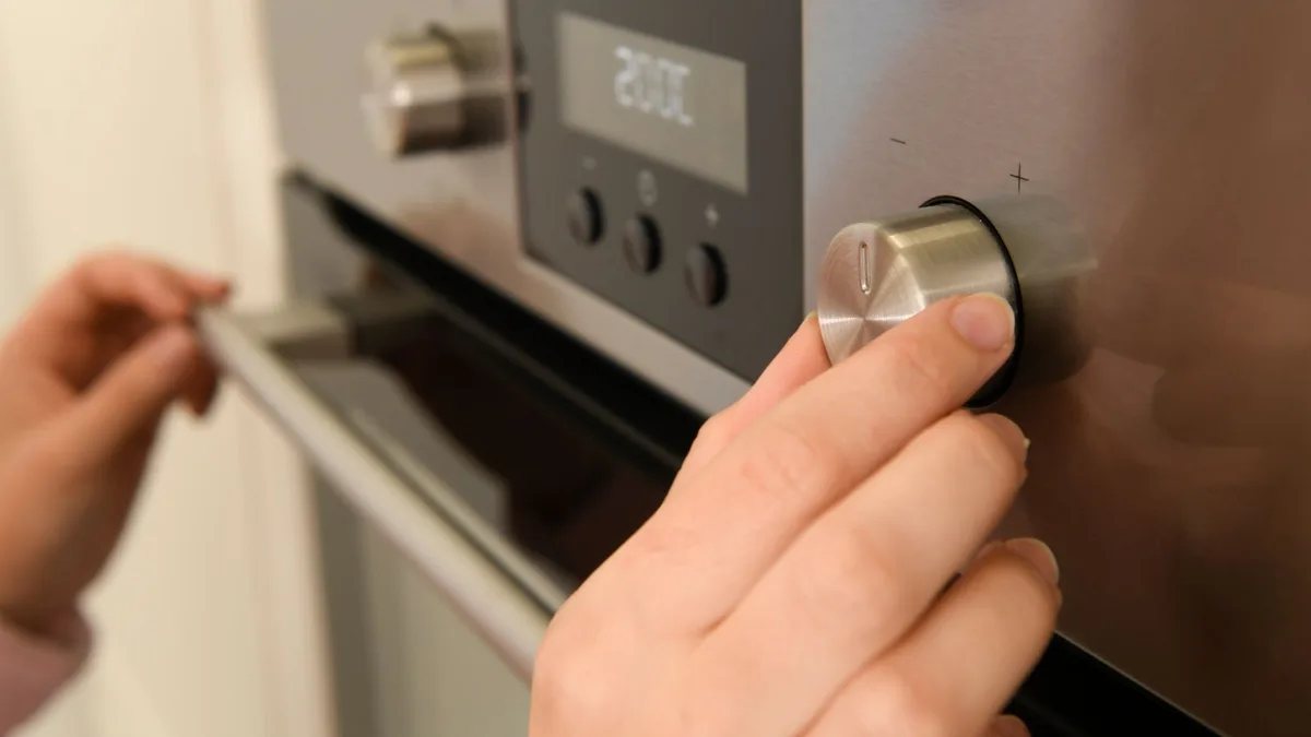 Mano girando el mando de temperatura de un horno eléctrico cuyo display marca 200 grados