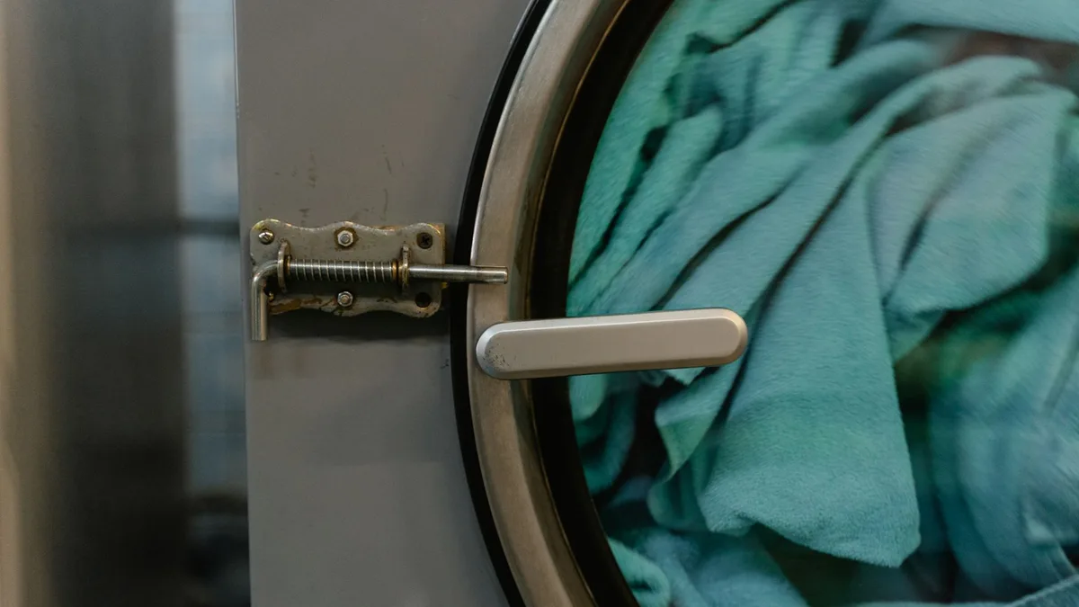 Detalle de la bisagra y el cierre de la puerta de una lavadora con ropa dentro