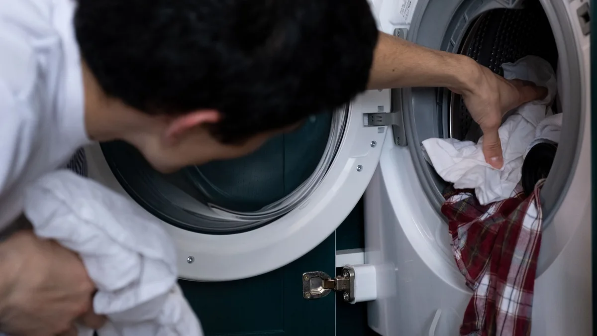 Persona agachada sacando ropa del tambor de una lavadora de carga frontal